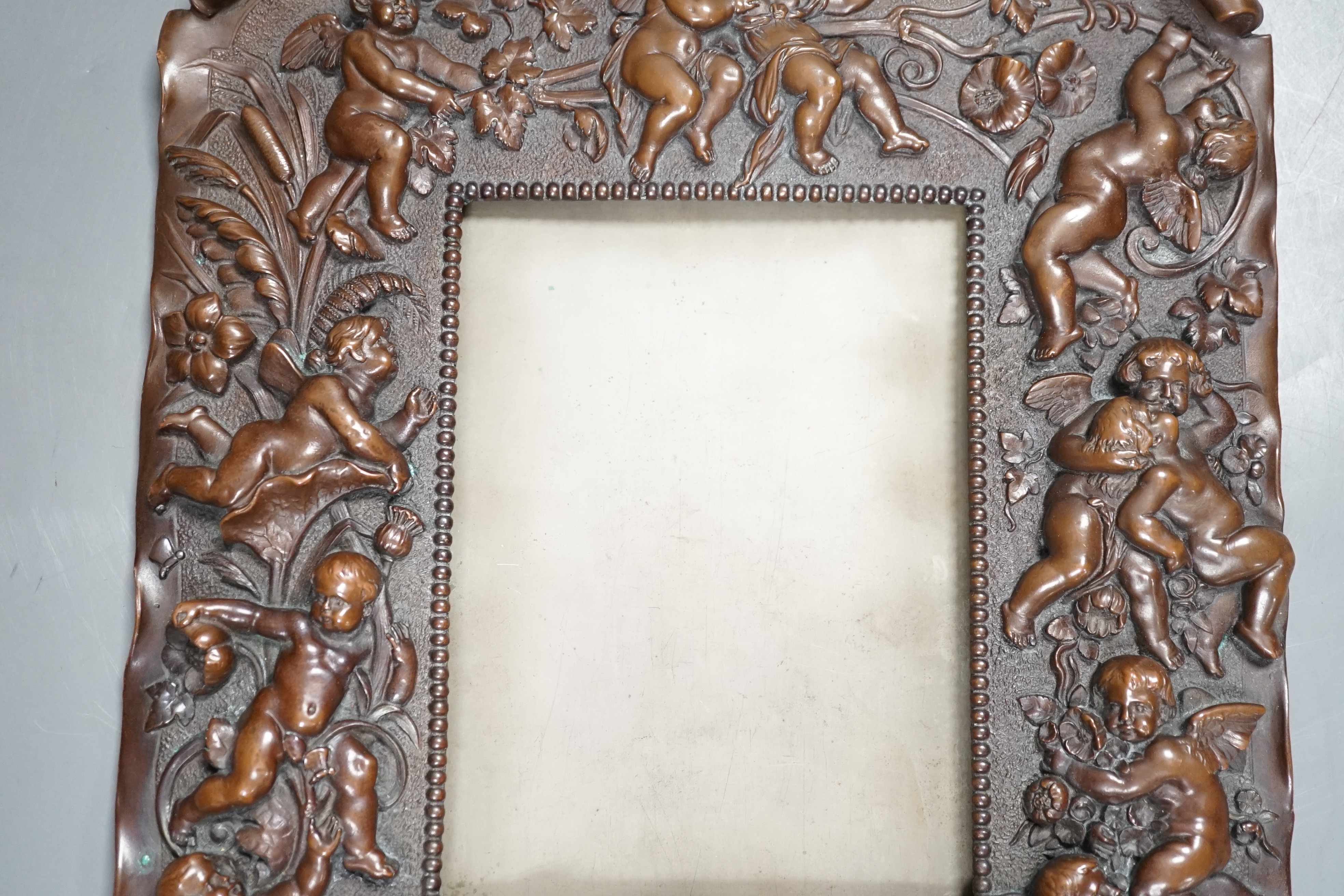 A bronzed copper frame decorated with putti, circa 1900. 28.5cm long